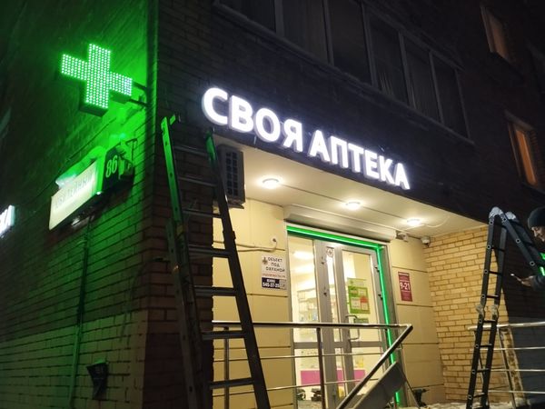 Световая вывеска аптеки с зелёным крестом после монтажа