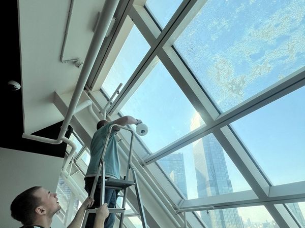 Монтажник на стремянке работает с наклонным фасадным остеклением